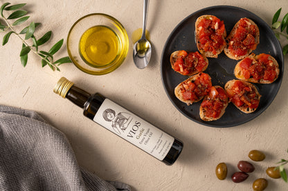 Bottle of VIOS garlic extra virgin olive oil with a plate of bruschetta, olives, and a bowl of oil