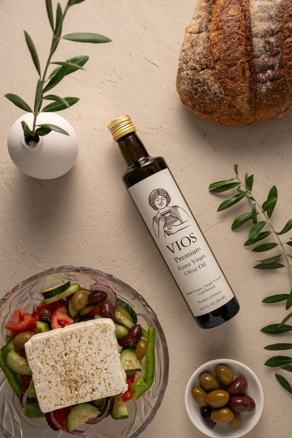 Bottle of VIOS premium extra virgin olive oil with a salad, bread, and bowl of olives on a table