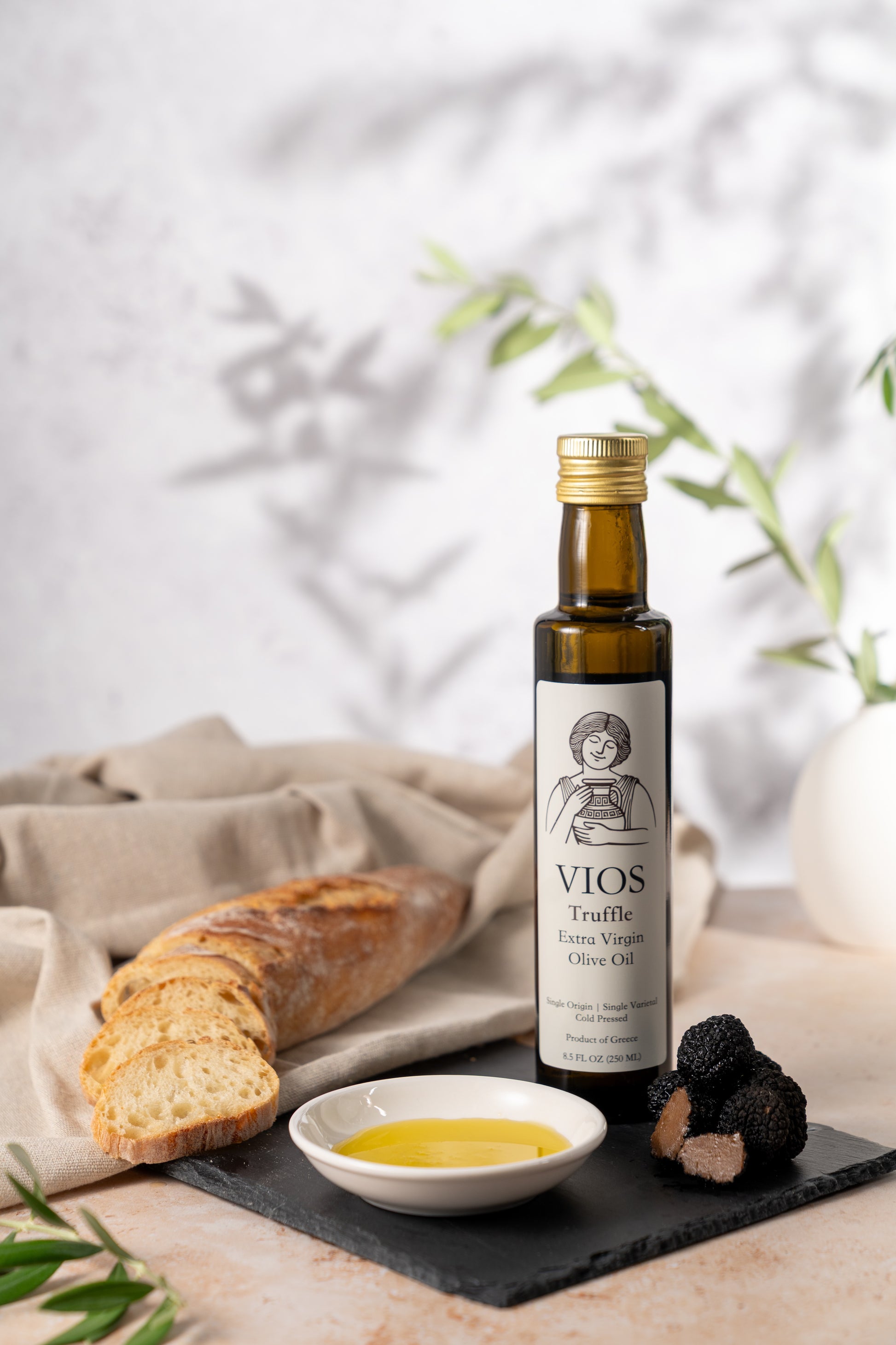 Bottle of VIOS truffle extra virgin olive oil with bread, truffles, and a saucer filled with olive oil on a table