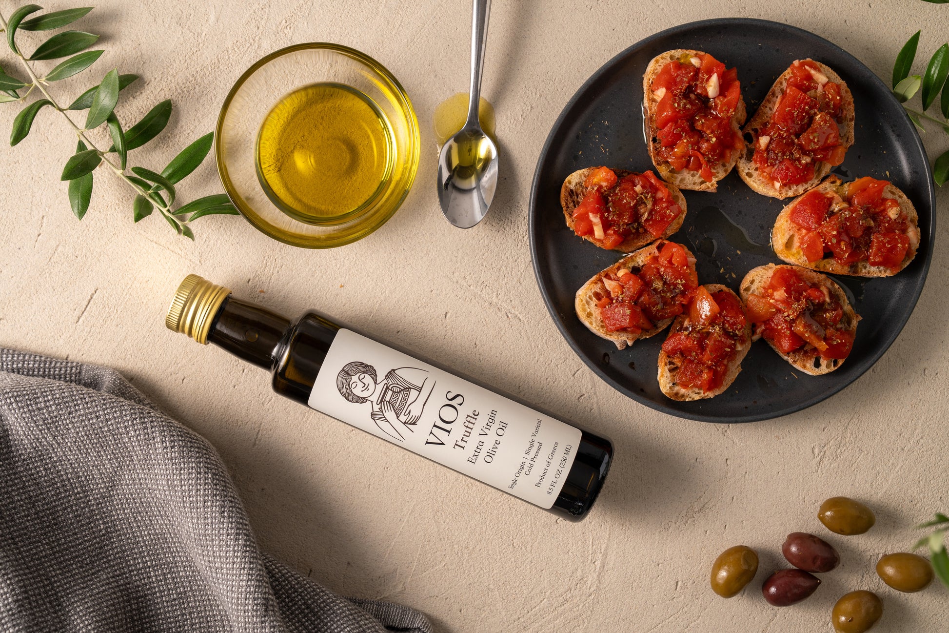Bottle of VIOS extra virgin olive oil with a plate of bruschetta, olives, and a bowl of olive oil.