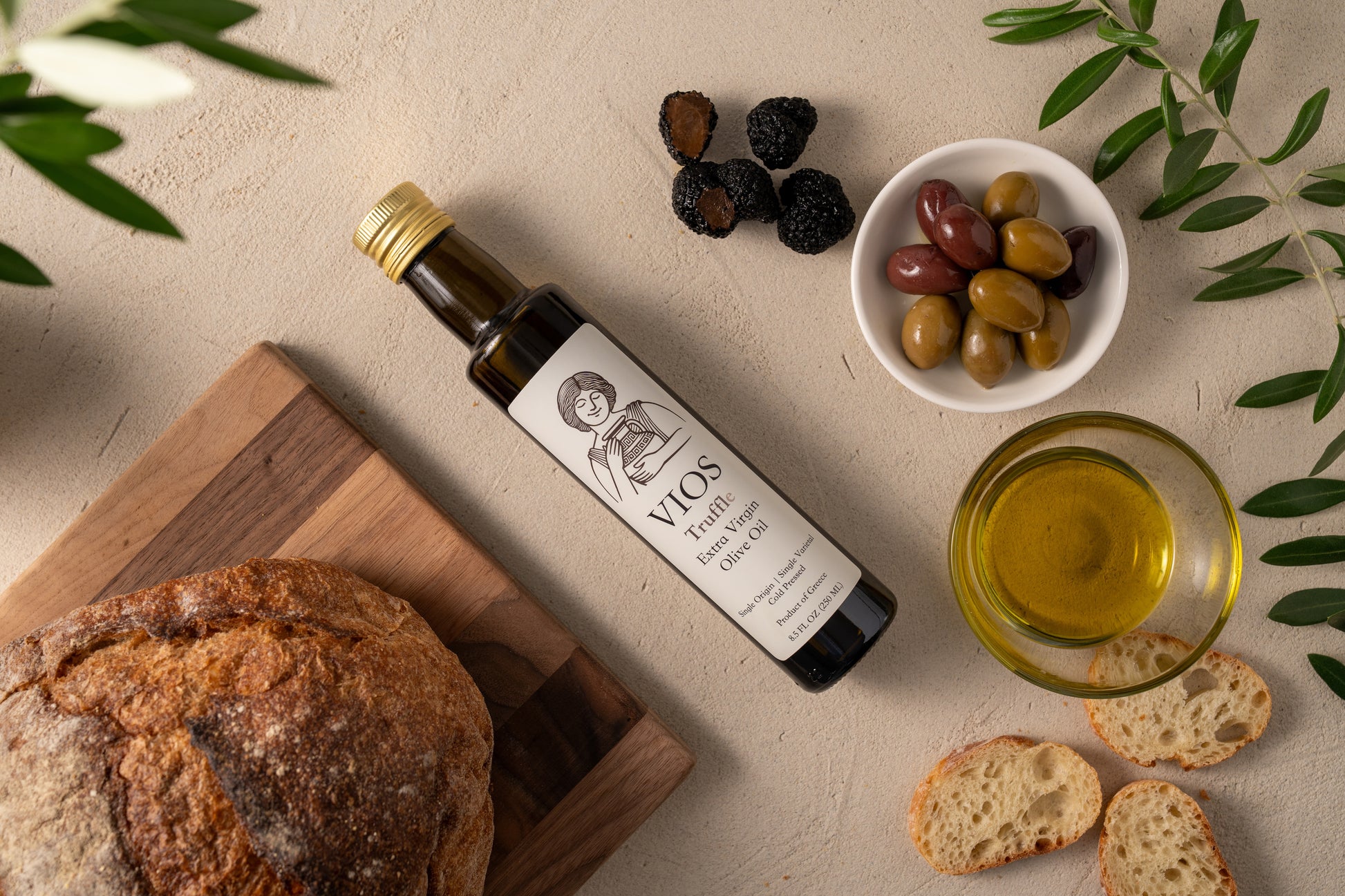 Bottle of Vios truffle extra virgin olive oil with bread, olives, truffles, and a bowl of olive oil.