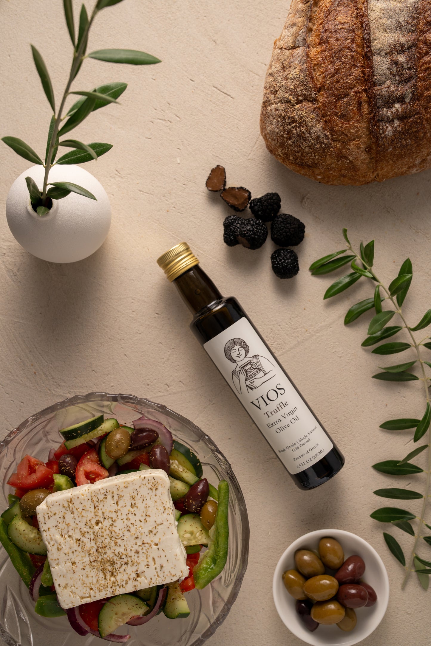 Bottle of VIOS truffle extra virgin olive oil with a salad, bread, and bowl of olives on a table.